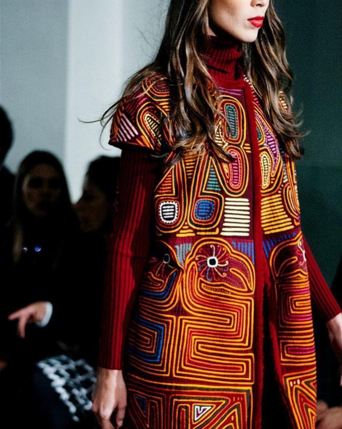 Woman wearing a red vest with vibrant, colorful geometric embroidery patterns while walking outdoors.