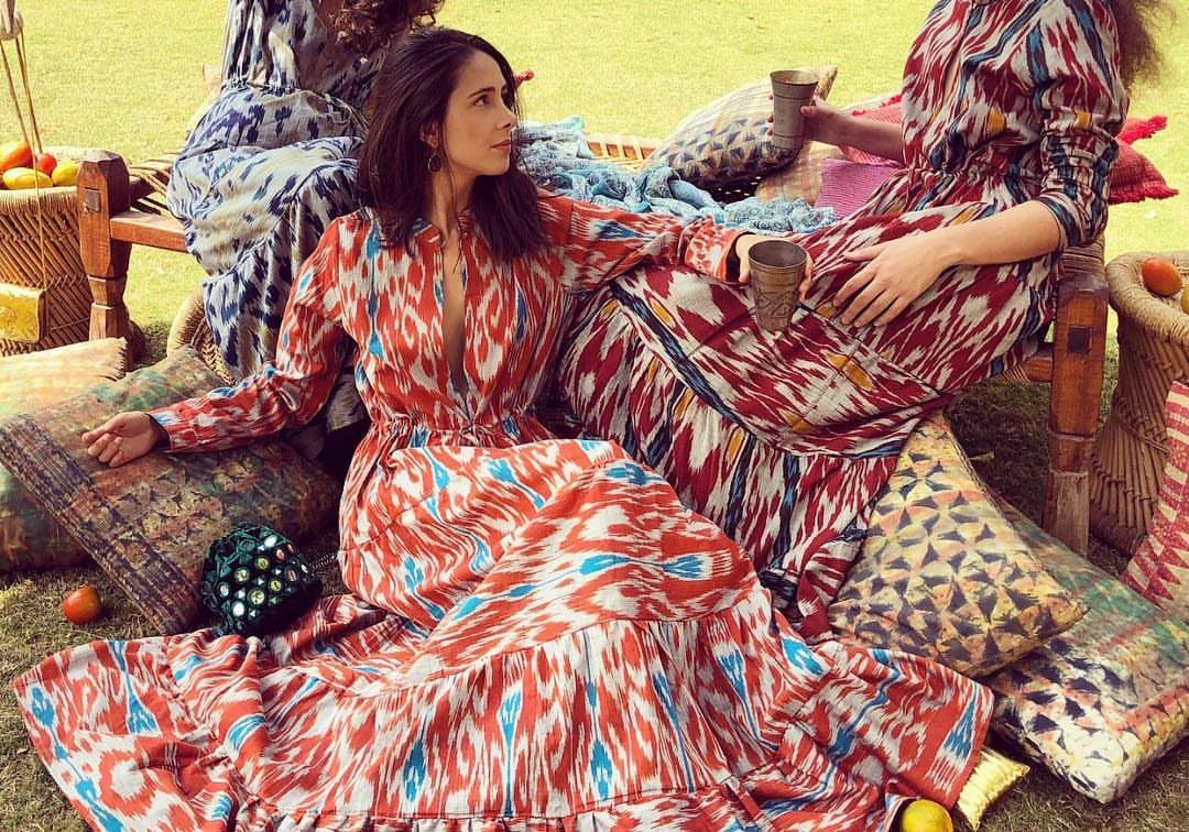 Women in vibrant red and blue ikat patterned dresses sitting on cushions outdoors.