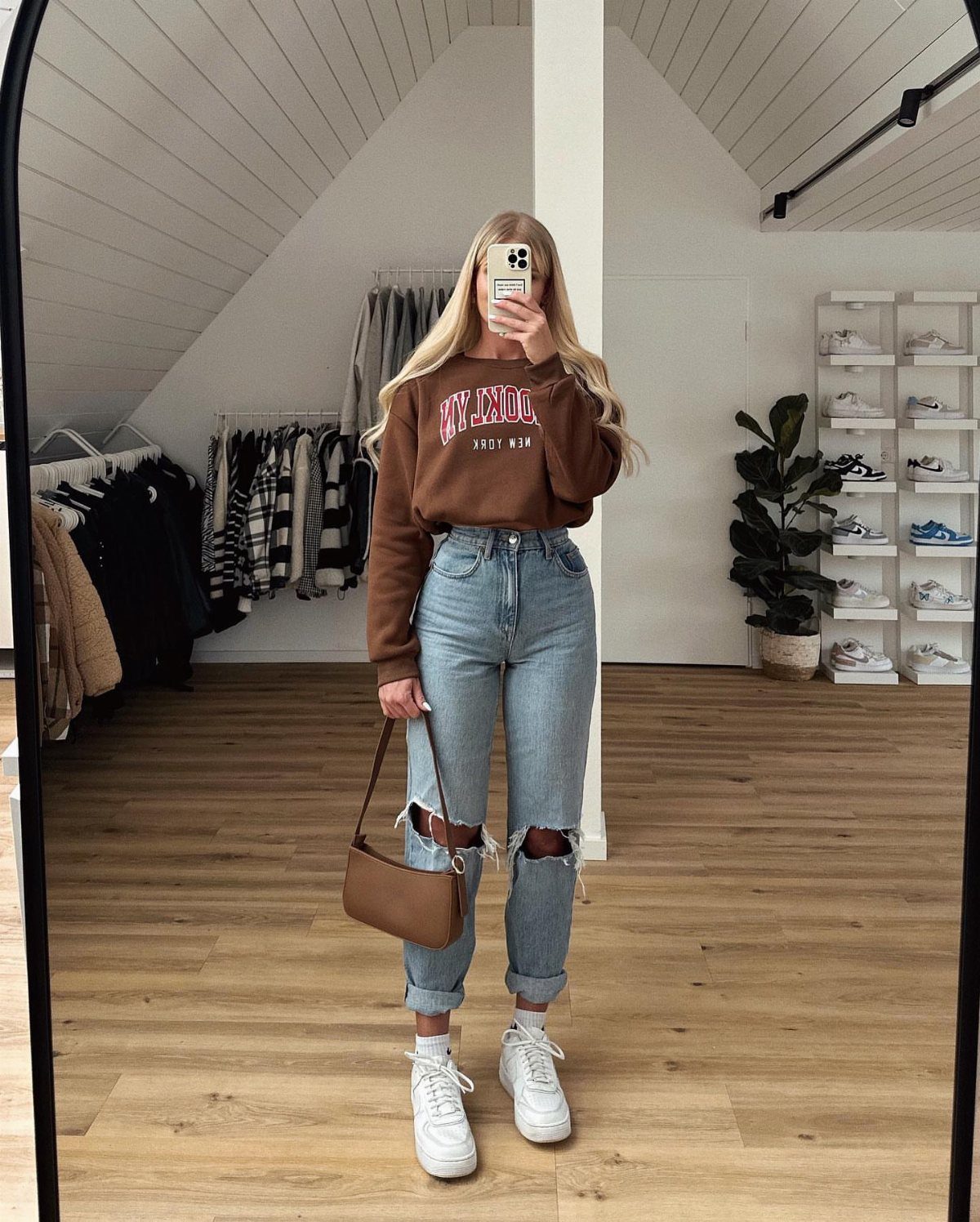 Woman in a brown cropped crew neck sweater and ripped blue jeans posing in a mirror.