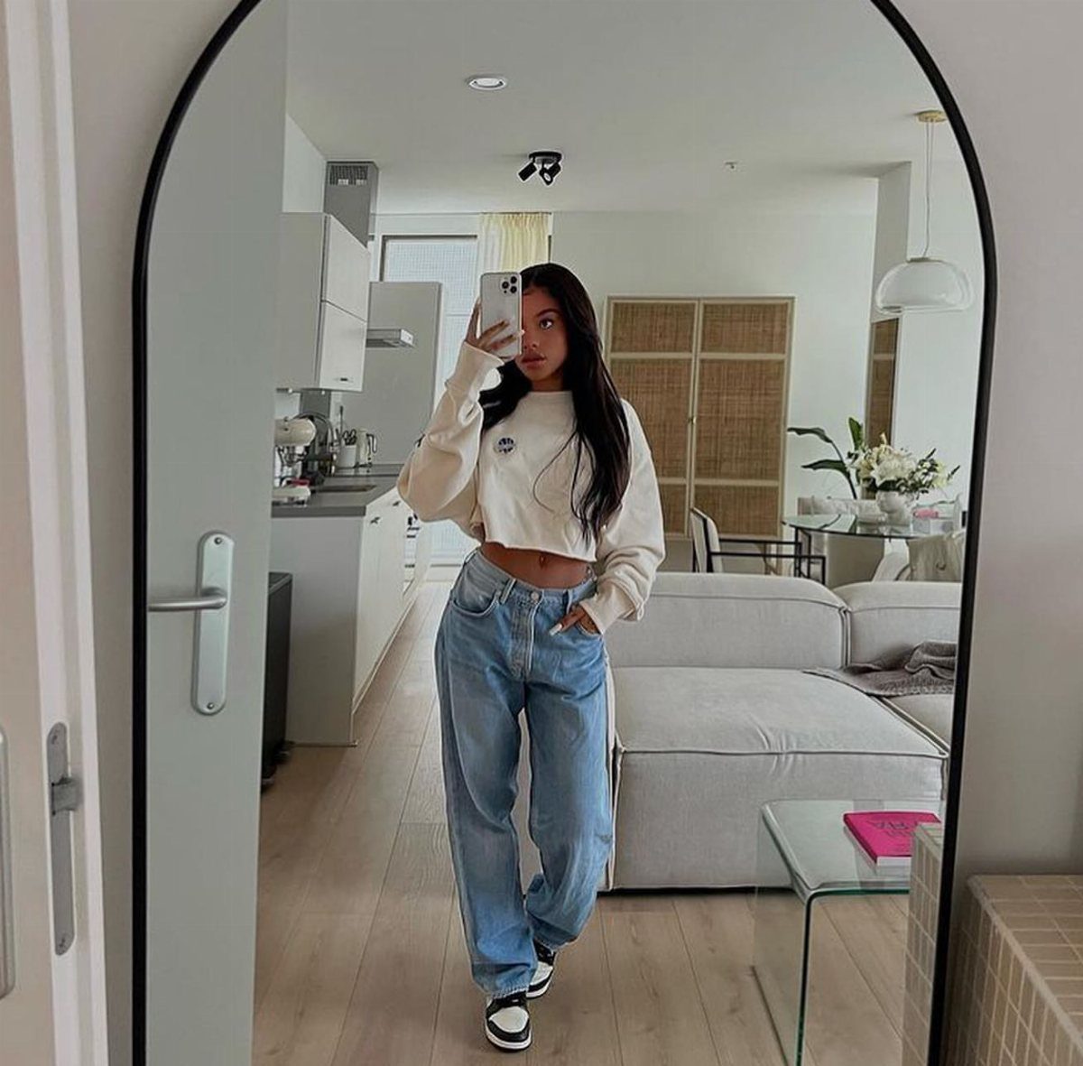 Woman in a cream cropped sweatshirt and light blue wide-leg jeans taking a mirror selfie.