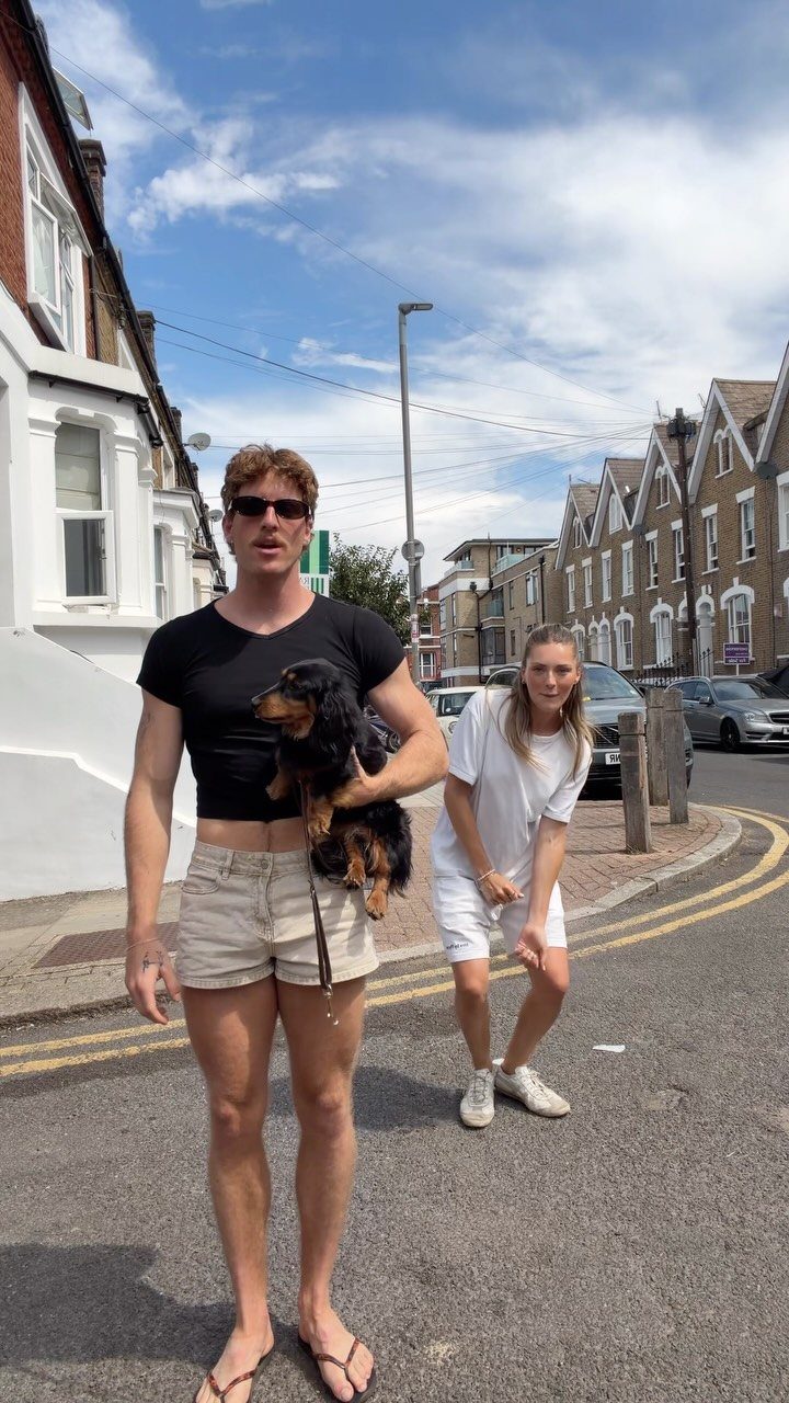A man wearing a black crop top holding a small dog on a sunny street.