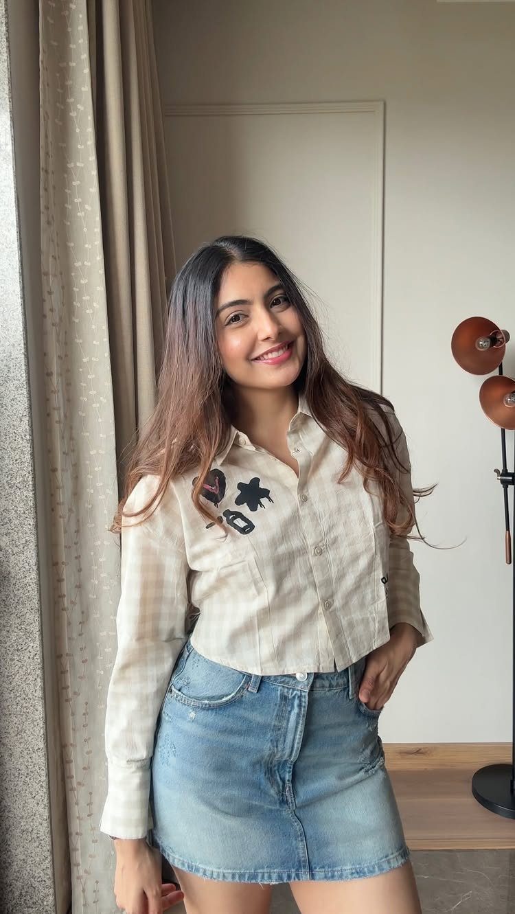 Smiling woman posing in a cream embroidered crop top and denim mini skirt.