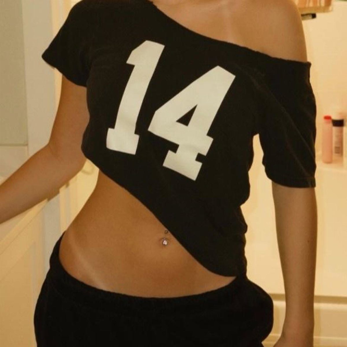 Person wearing a black off-the-shoulder crop top featuring a large white number 14.