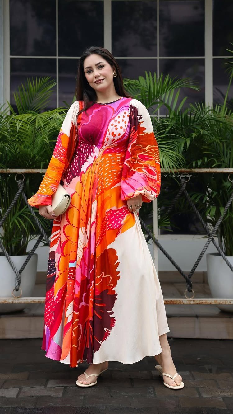 Woman posing in a vibrant, large-scale floral print midi dress with orange and pink patterns.