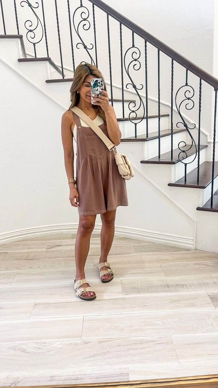 Woman in a brown sleeveless romper and beige sandals posing for a mirror selfie.