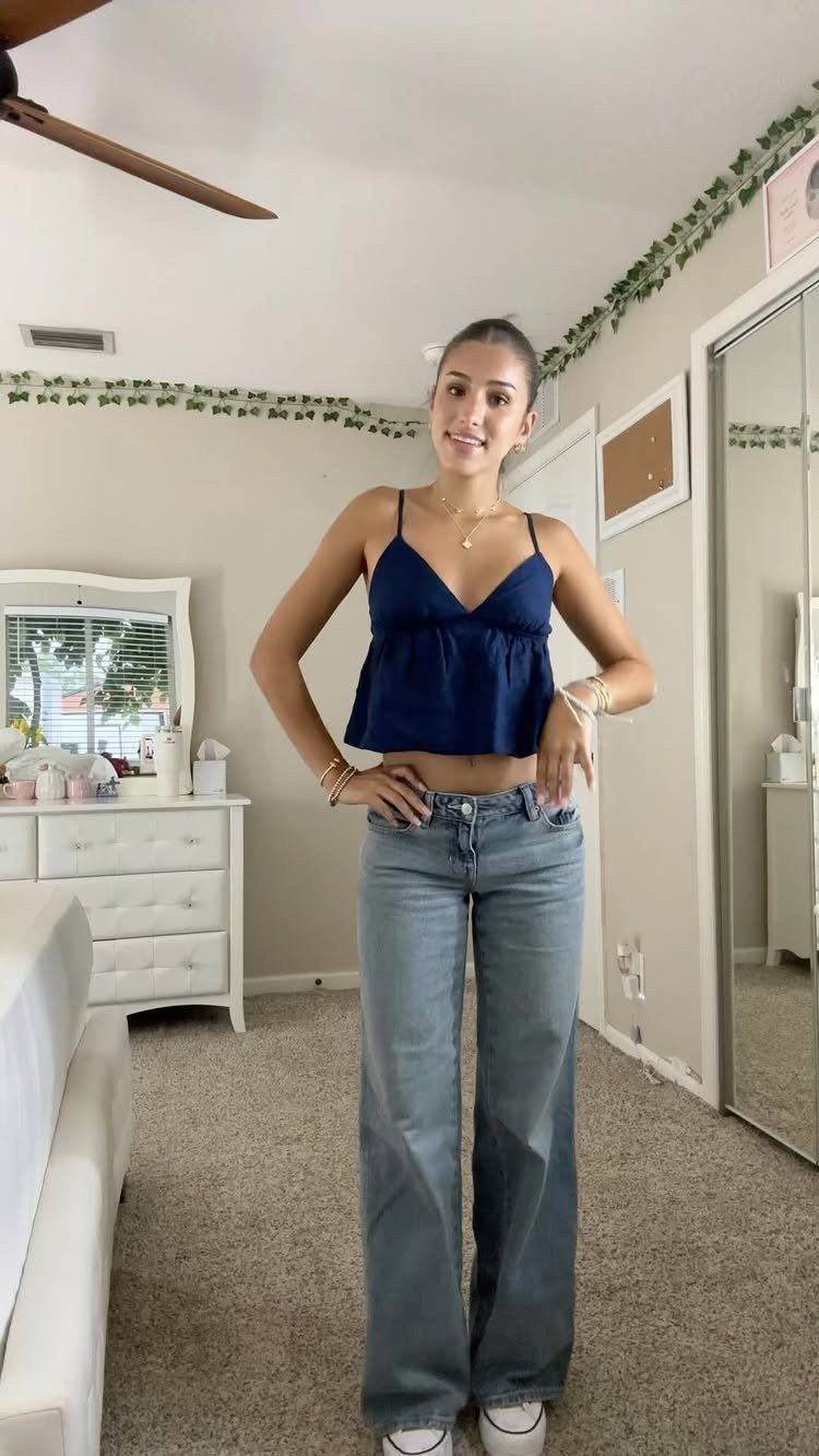Young woman posing in a navy blue cropped top and wide-leg denim jeans.
