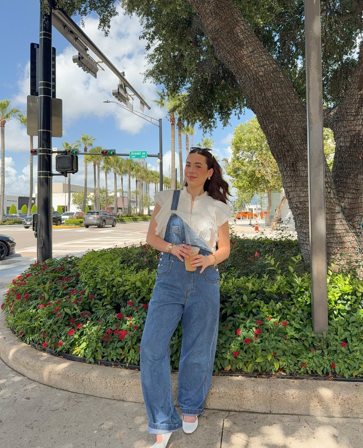 Woman wearing blue denim high-rise loose flare overalls and a white ruffled top standing outdoors.