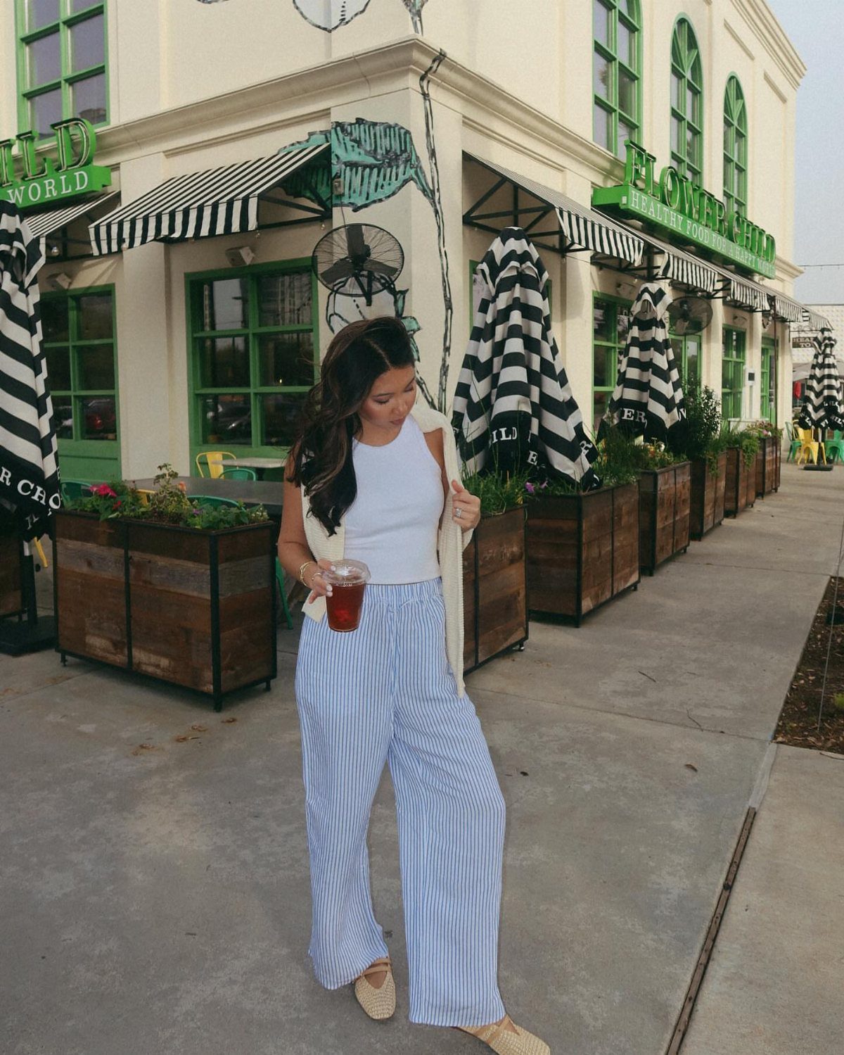Woman in a white top and striped wide-leg trousers standing on a city sidewalk.