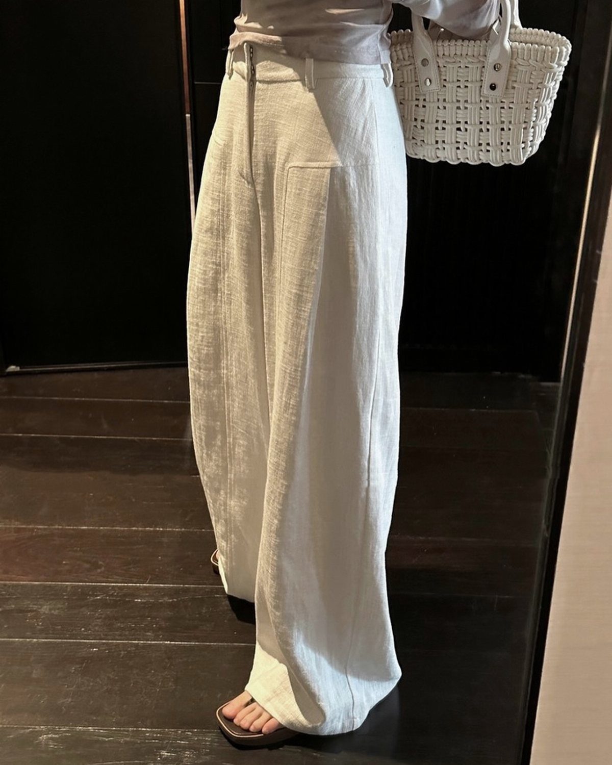 Person wearing white wide-leg linen trousers and holding a white woven basket bag.