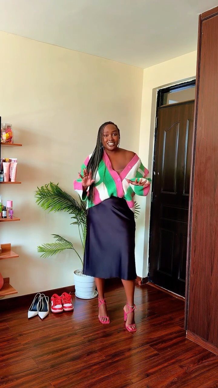 Woman posing in a striped chunky sweater and a black satin midi skirt.