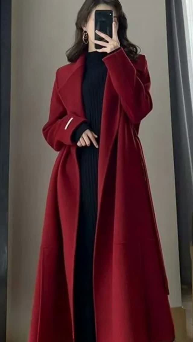 A person wearing a long red coat and a black turtleneck sweater taking a mirror selfie.