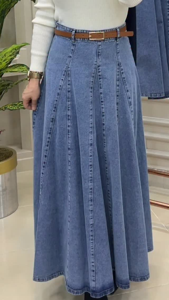 A person wearing a long pleated light-wash denim maxi skirt with a brown belt.