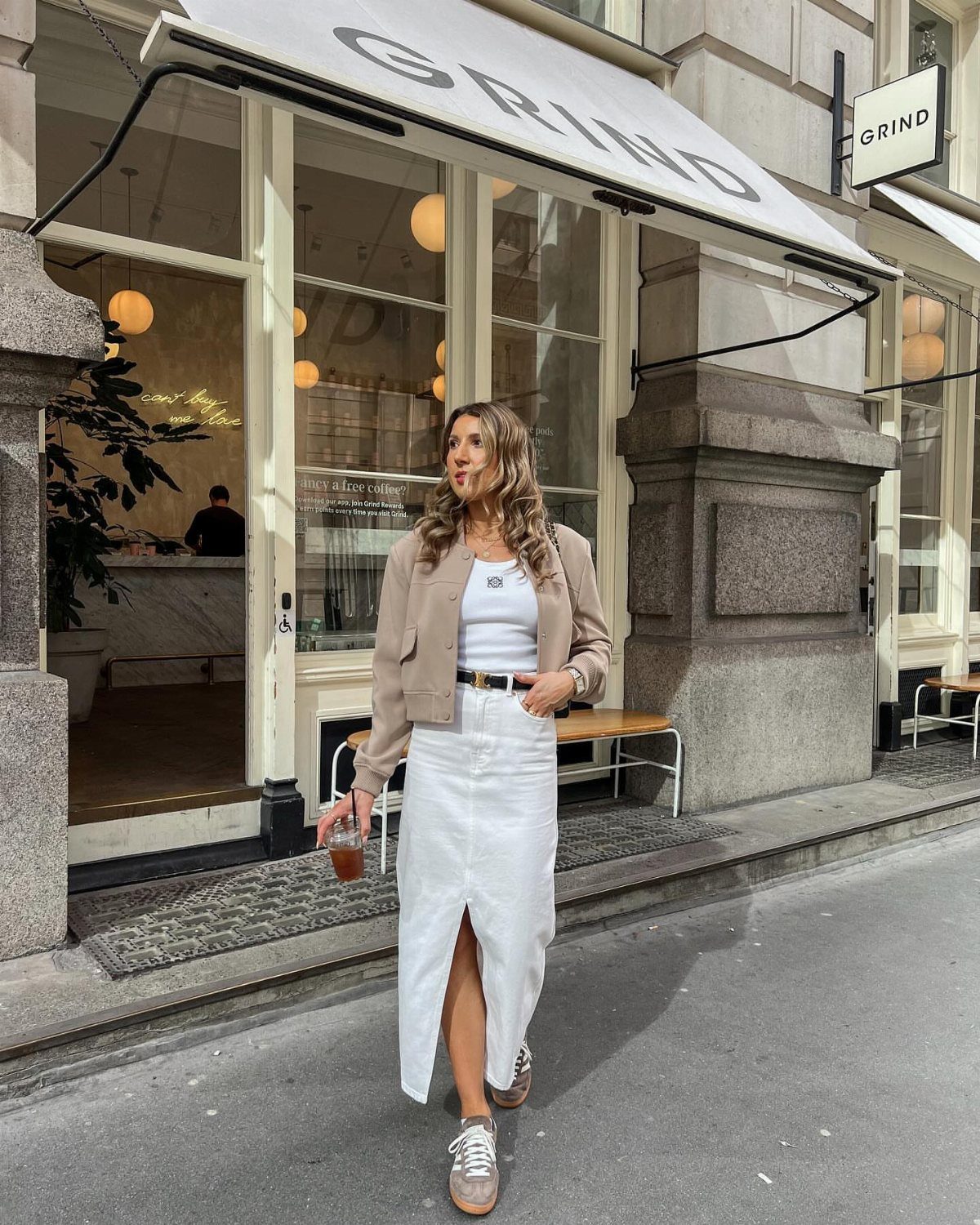 Woman walking on a city street wearing a white denim midi skirt and a tan blazer.