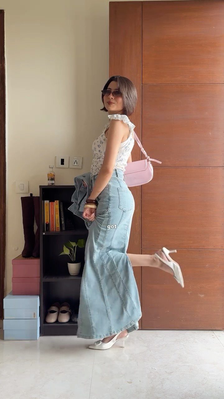 Woman wearing a light-wash denim mermaid skirt and white floral top posing indoors.
