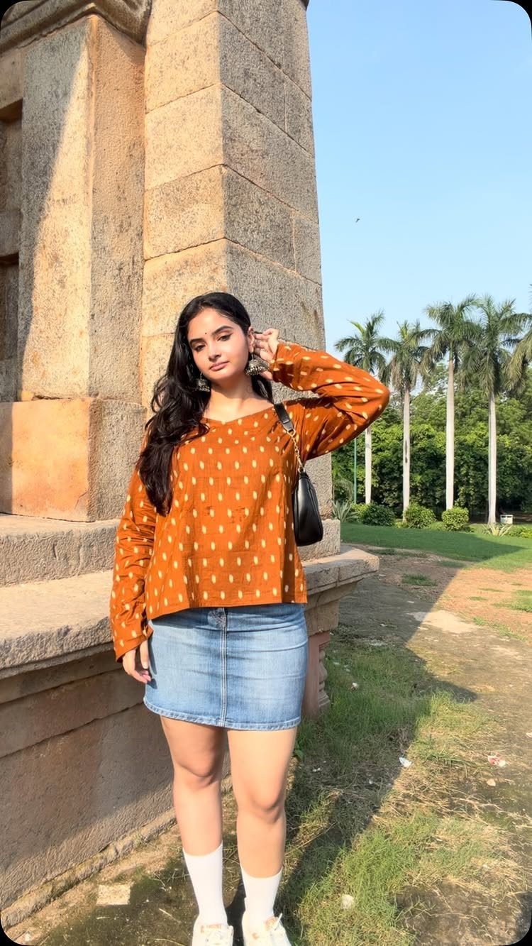 Woman wearing an orange patterned top and a light blue denim mini skirt outdoors.