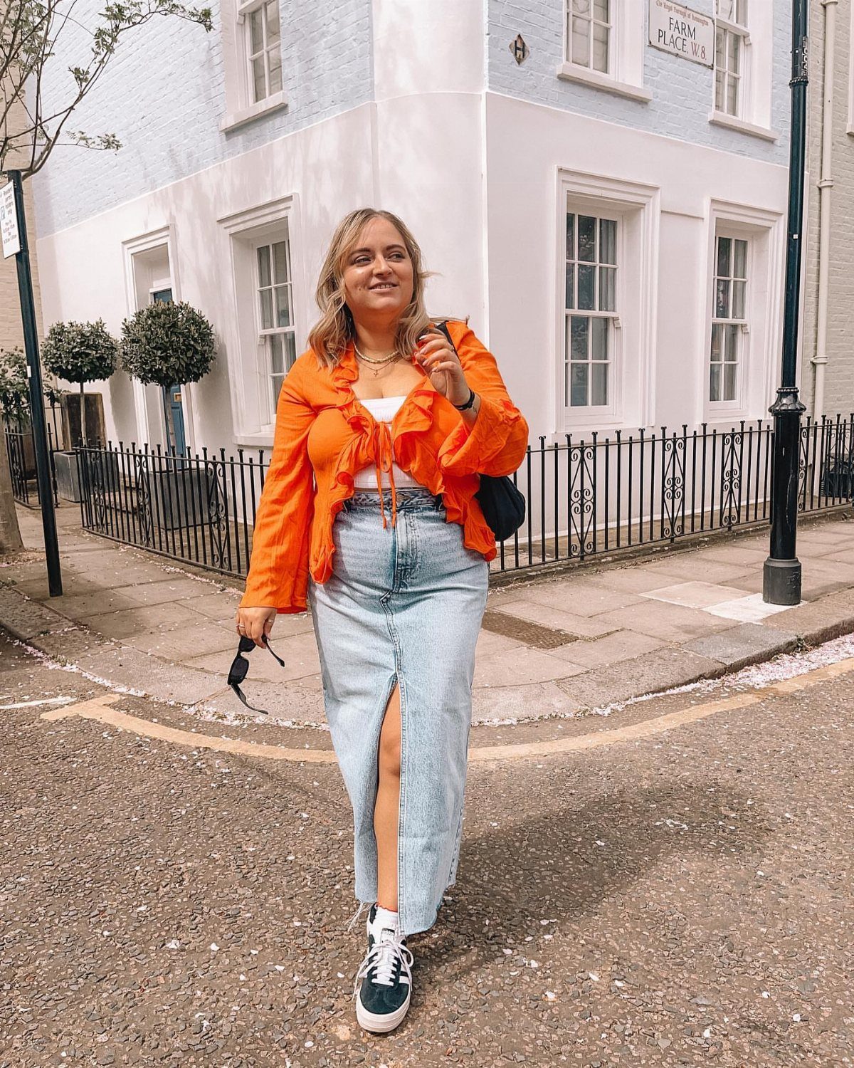 Woman wearing a long denim skirt paired with a bright orange lightweight shirt.