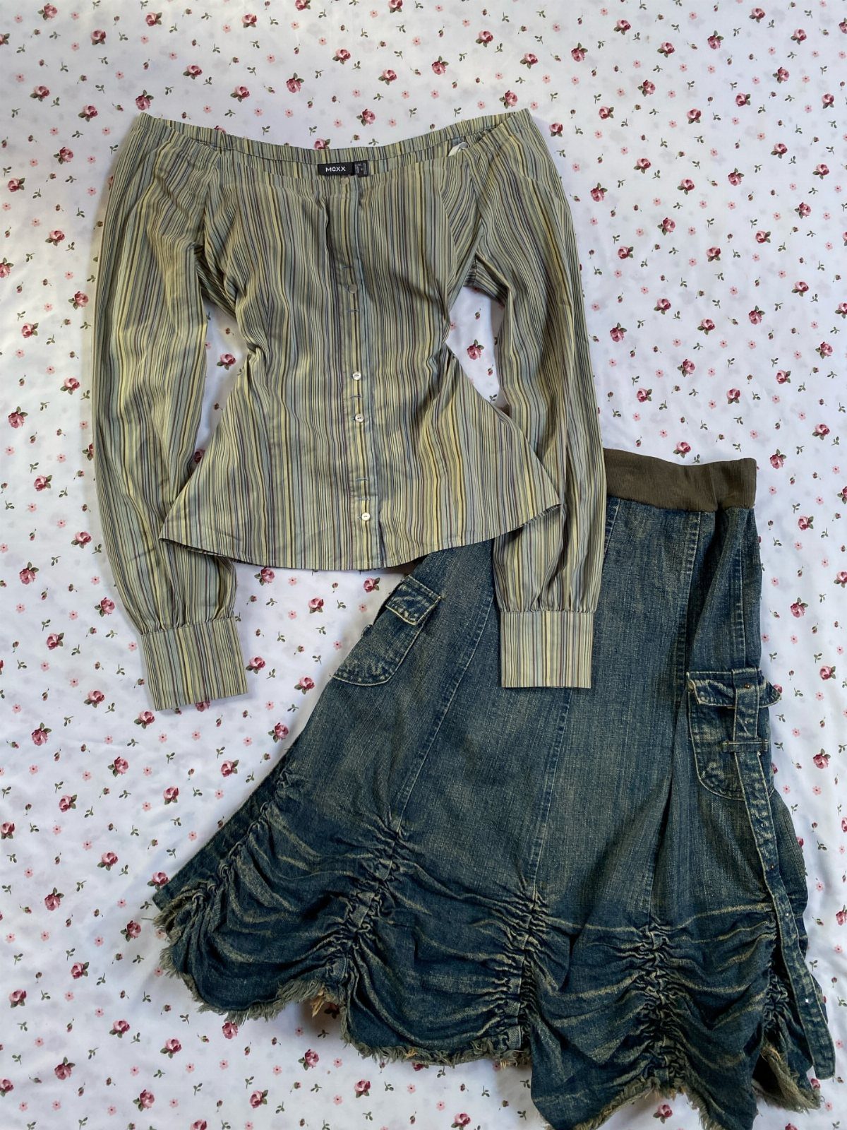 A striped off-the-shoulder blouse and a ruched denim skirt laid on floral bedding.