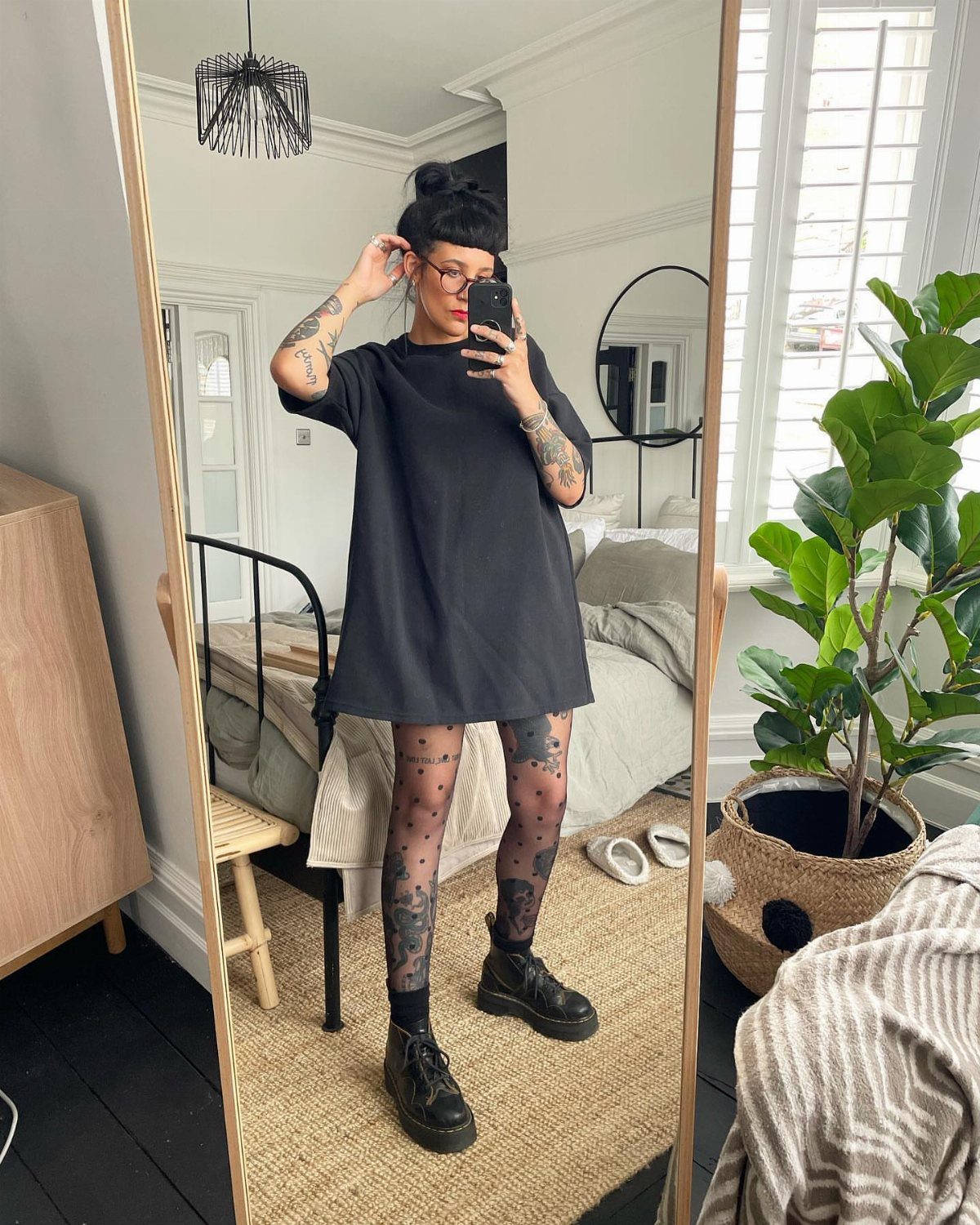 Woman in an oversized black dress and combat boots posing for a mirror selfie.