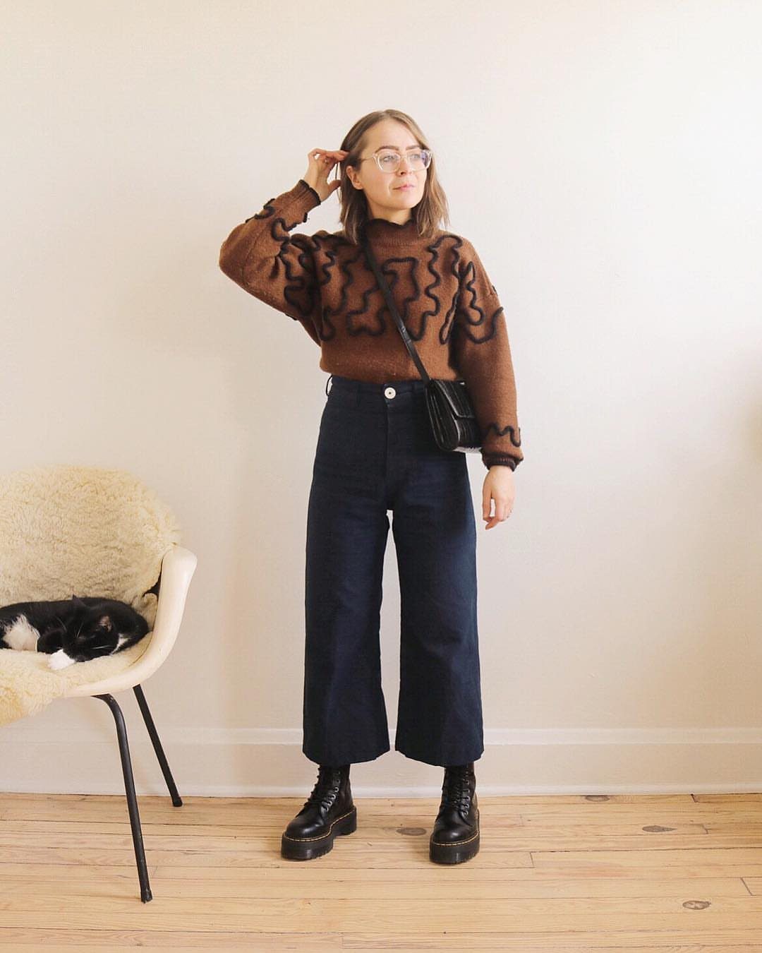 A woman posing in a brown sweater, dark wide-leg pants, and black platform boots.