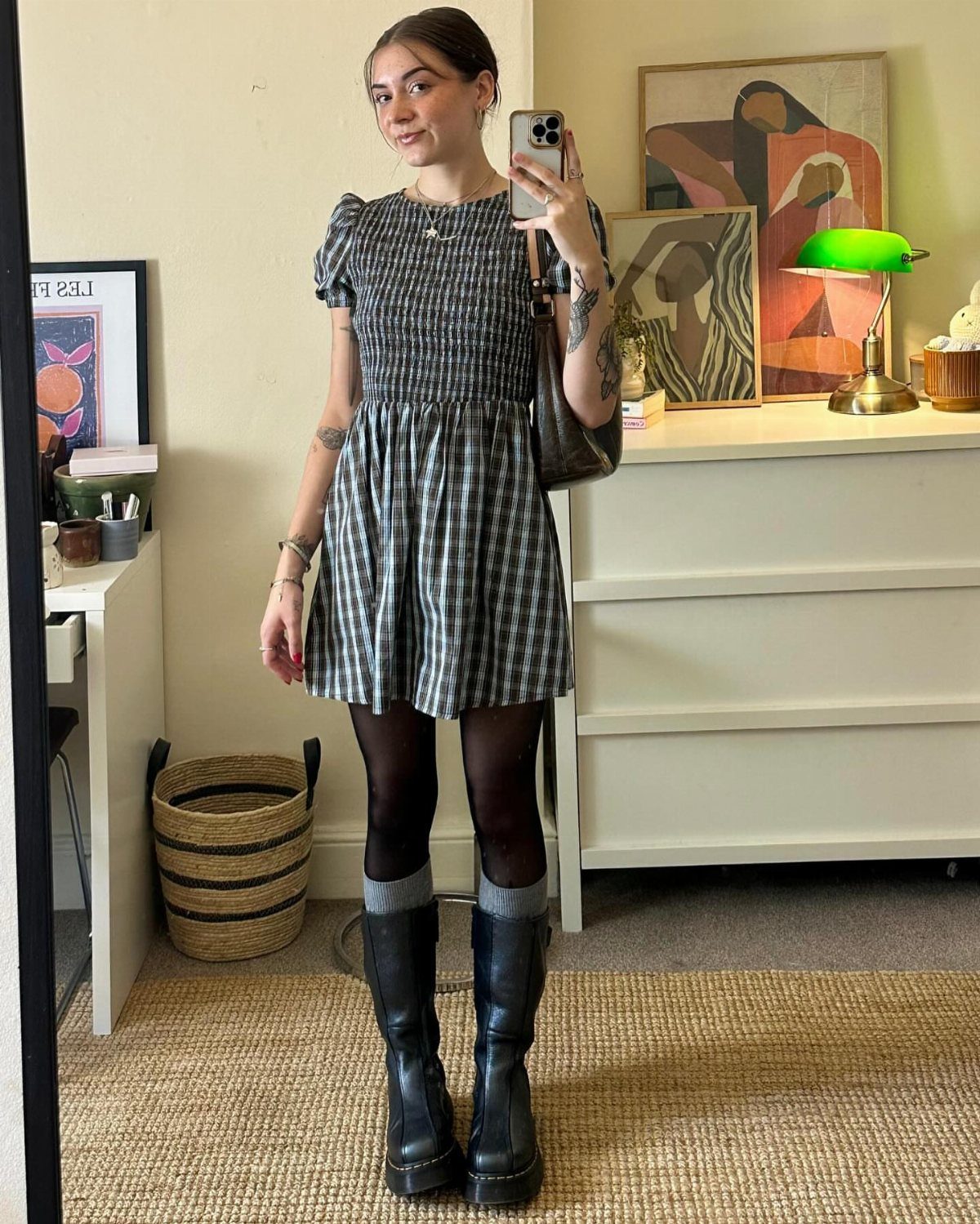 Woman in a checkered smocked dress, black tights, and black combat boots posing for a mirror selfie.