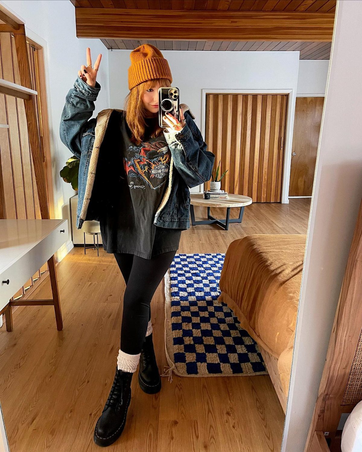 Woman in an oversized graphic t-shirt, denim jacket, and black boots posing for a mirror selfie.