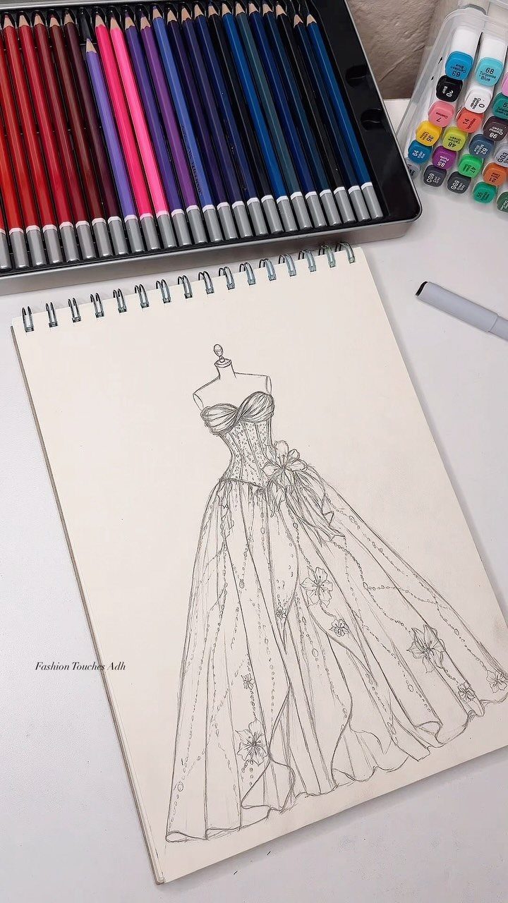A detailed black and white sketch of a ball gown in a spiral-bound sketchbook.