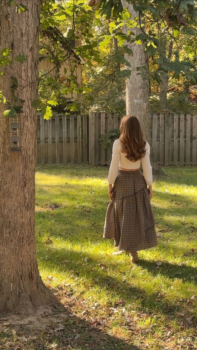 A woman wearing a white top and a long patterned maxi skirt standing in a sunny yard.