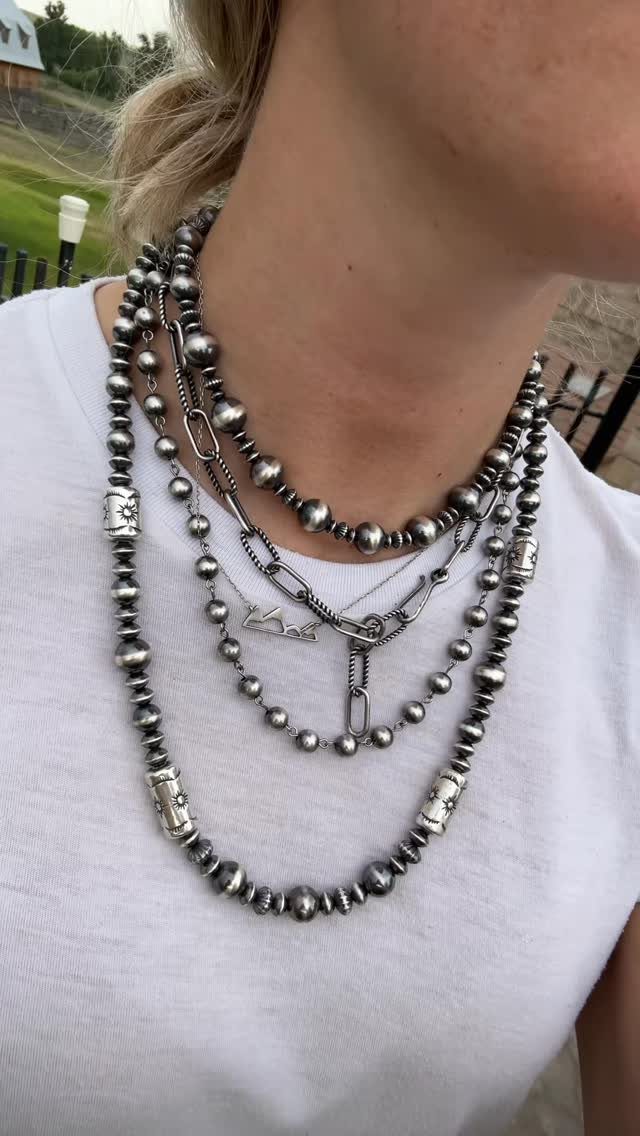 Layered silver beaded and chain necklaces worn over a white t-shirt.