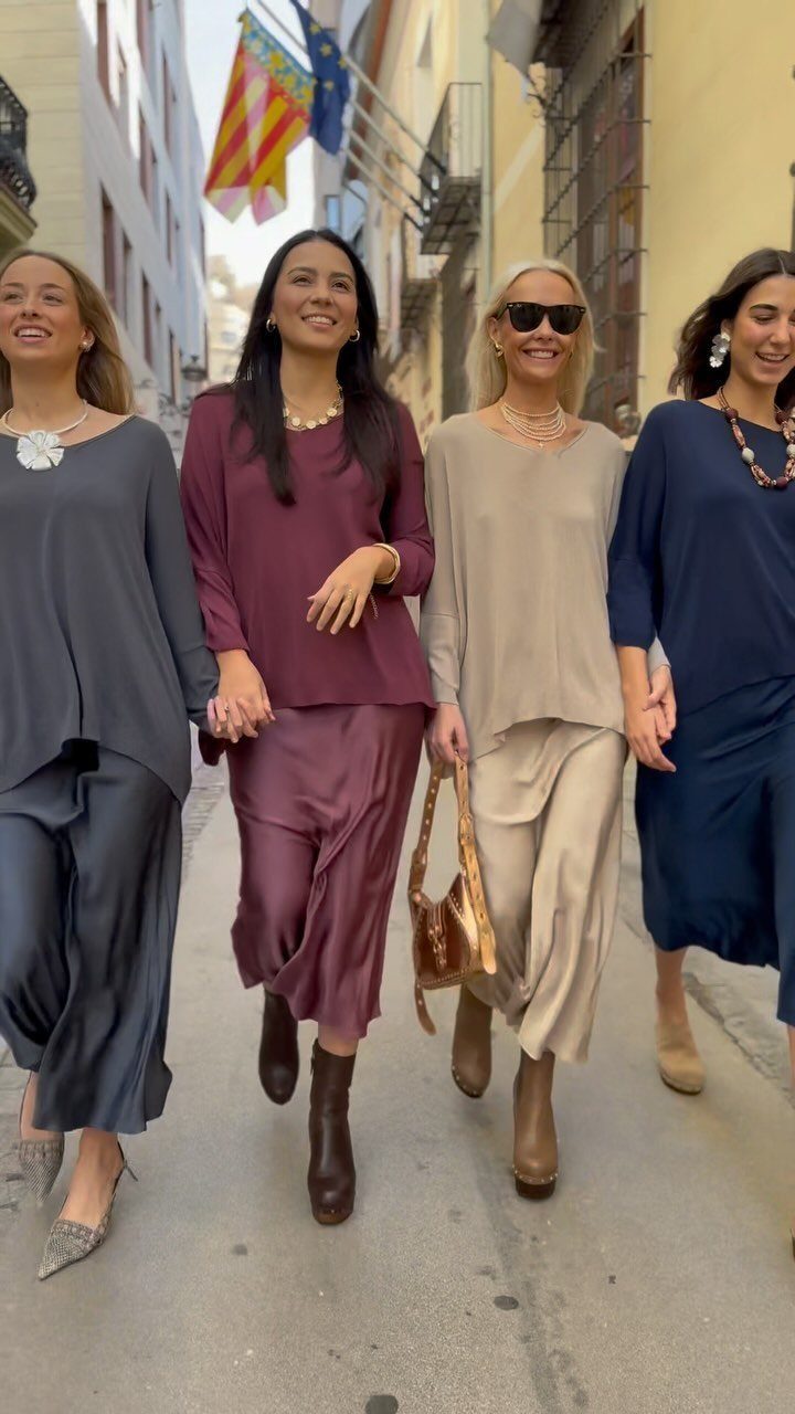 Four women walking down a street wearing loose tops and long satin skirts.