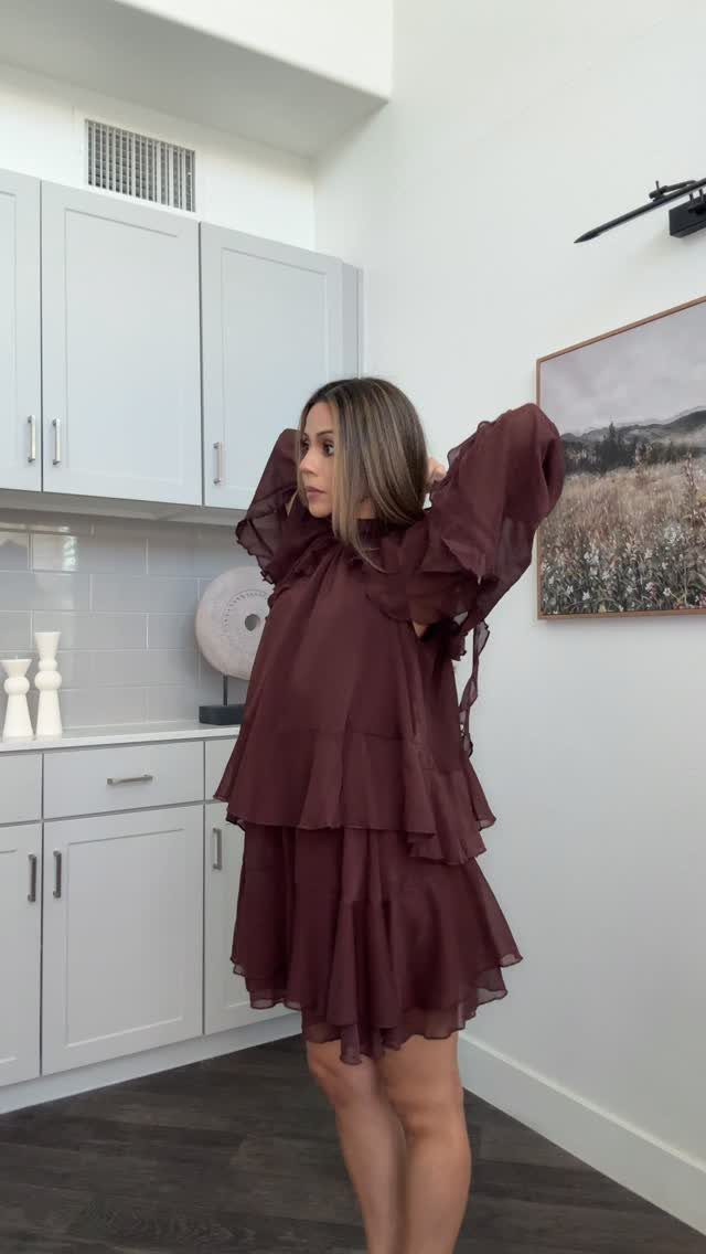 A woman posing in a maroon tiered mini dress with large ruffled sleeves.
