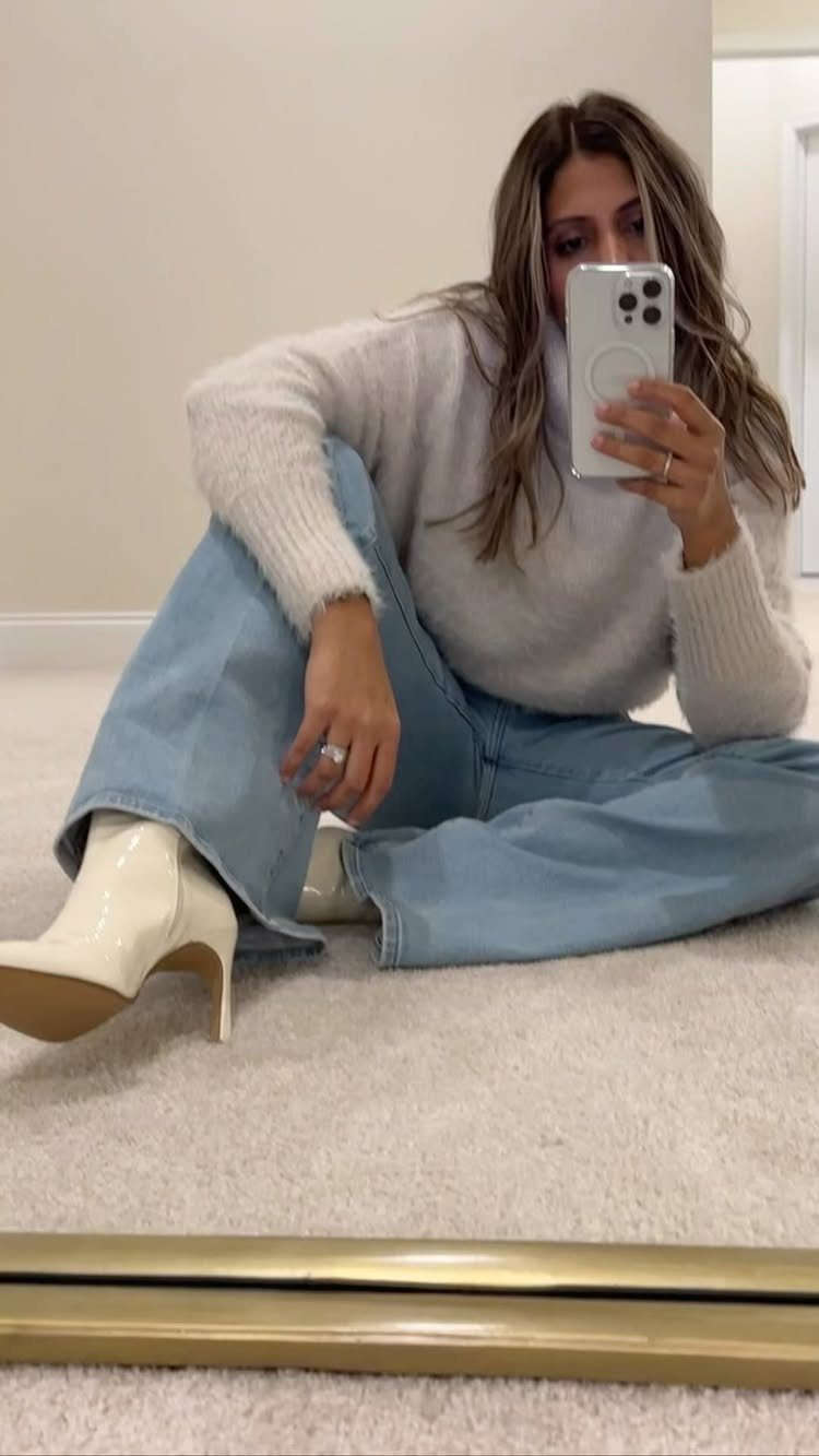Woman in a grey turtleneck, wide-leg jeans, and cream boots sitting on the floor.