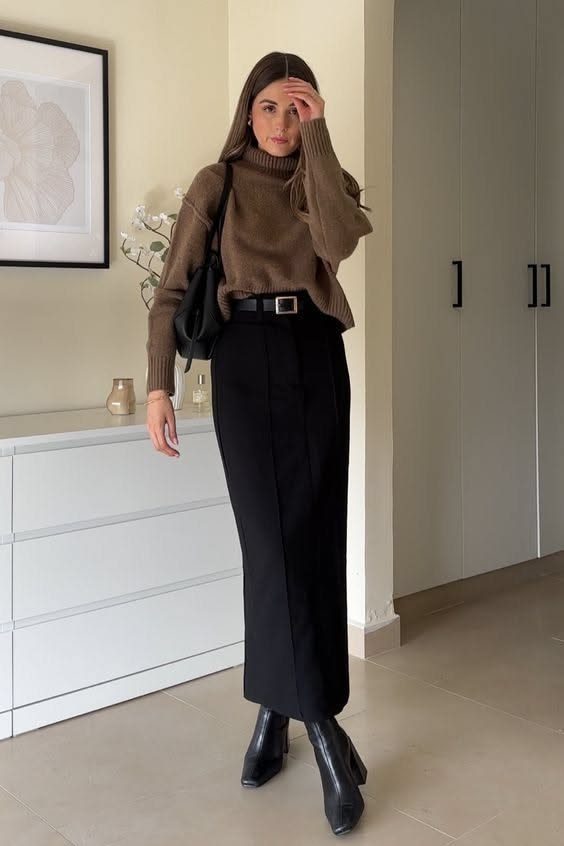A woman wearing a brown turtleneck sweater and a long black maxi skirt with black boots.