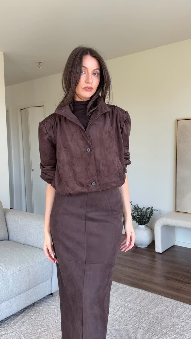 A woman posing in a dark brown suede jacket and matching long suede skirt.