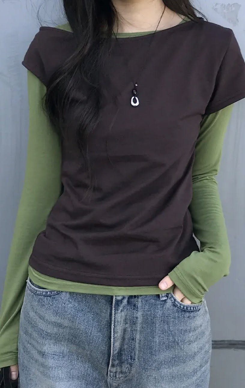 Person wearing a dark brown t-shirt layered over a long-sleeved olive green shirt and blue jeans.