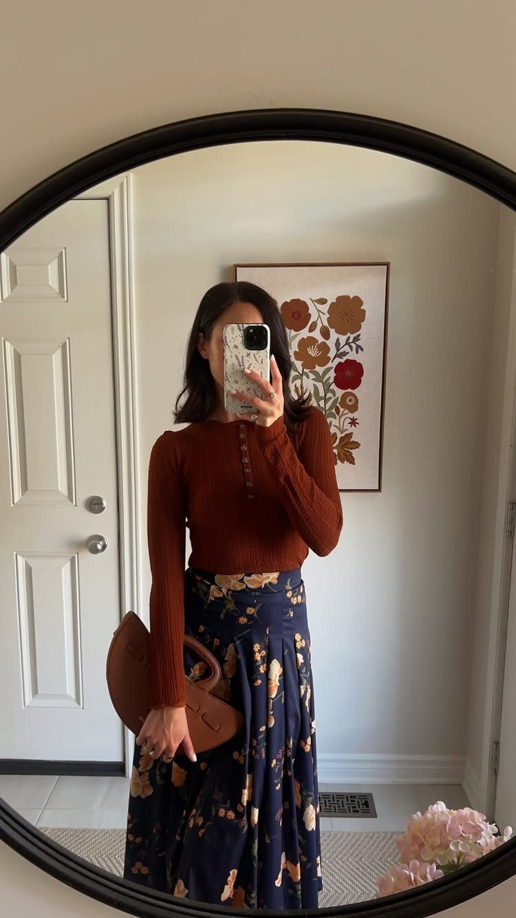 A woman in a rust top and navy floral skirt posing for a mirror selfie.