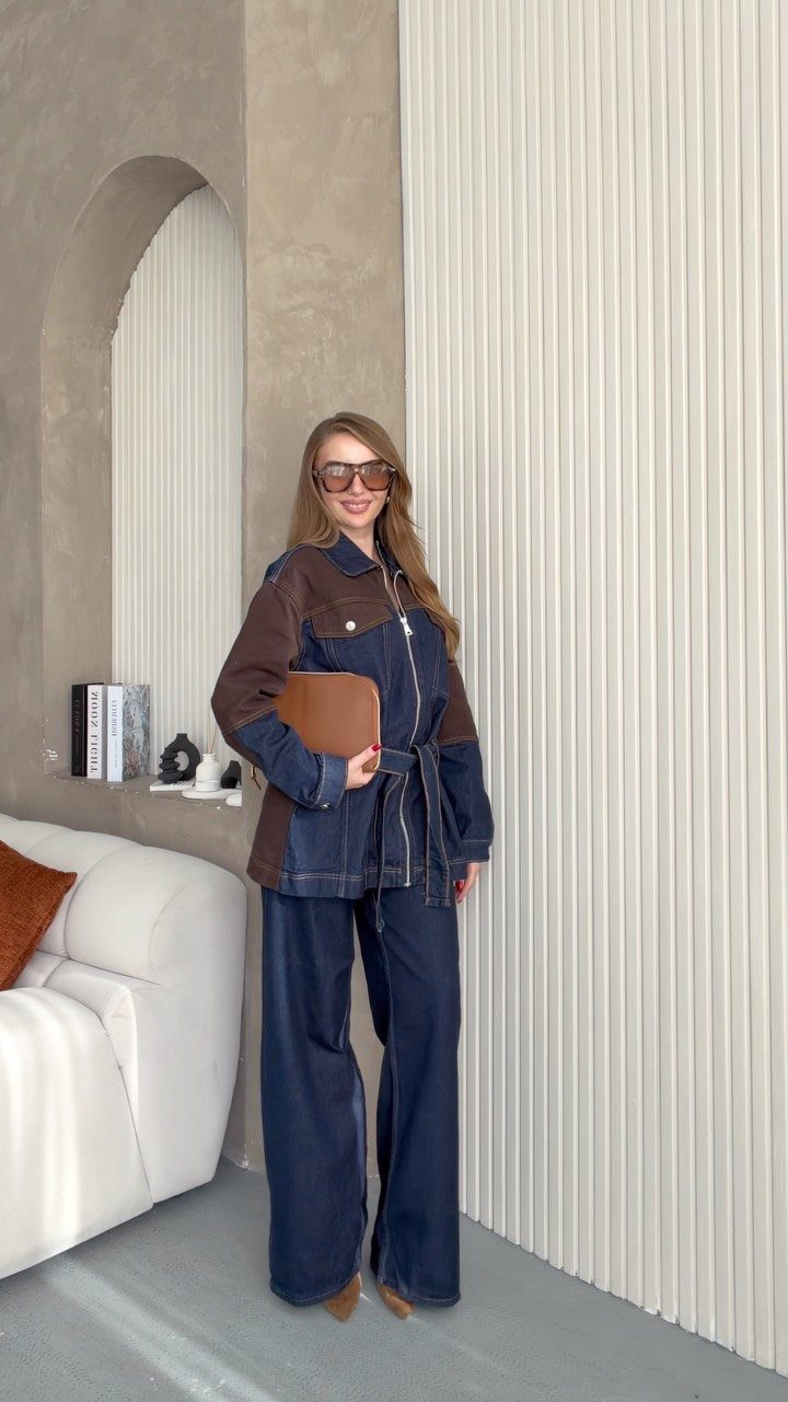 Woman posing in a denim jacket and matching wide-leg denim trousers while holding a brown clutch.