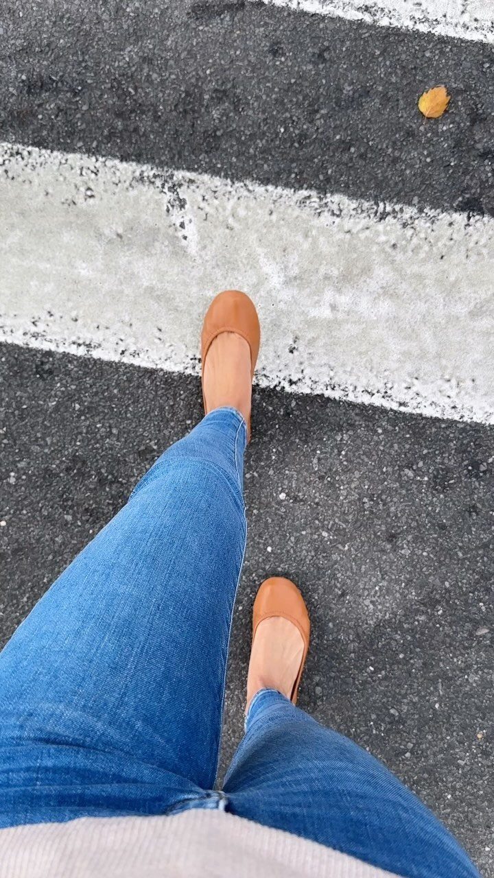 Person wearing blue jeans and tan leather ballet flats on a striped asphalt surface.