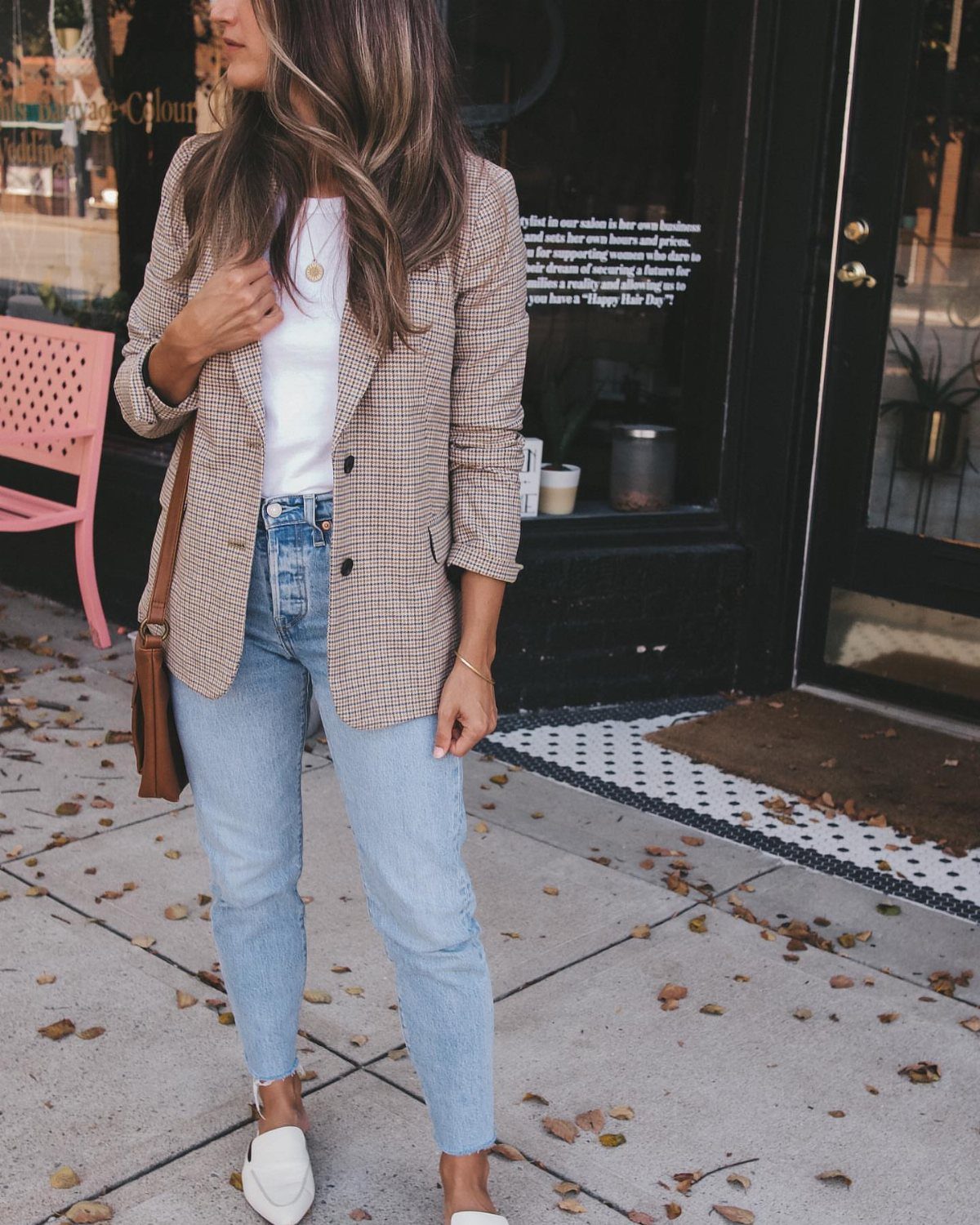 Woman wearing a brown checkered blazer, white top, and light blue denim jeans standing outdoors.