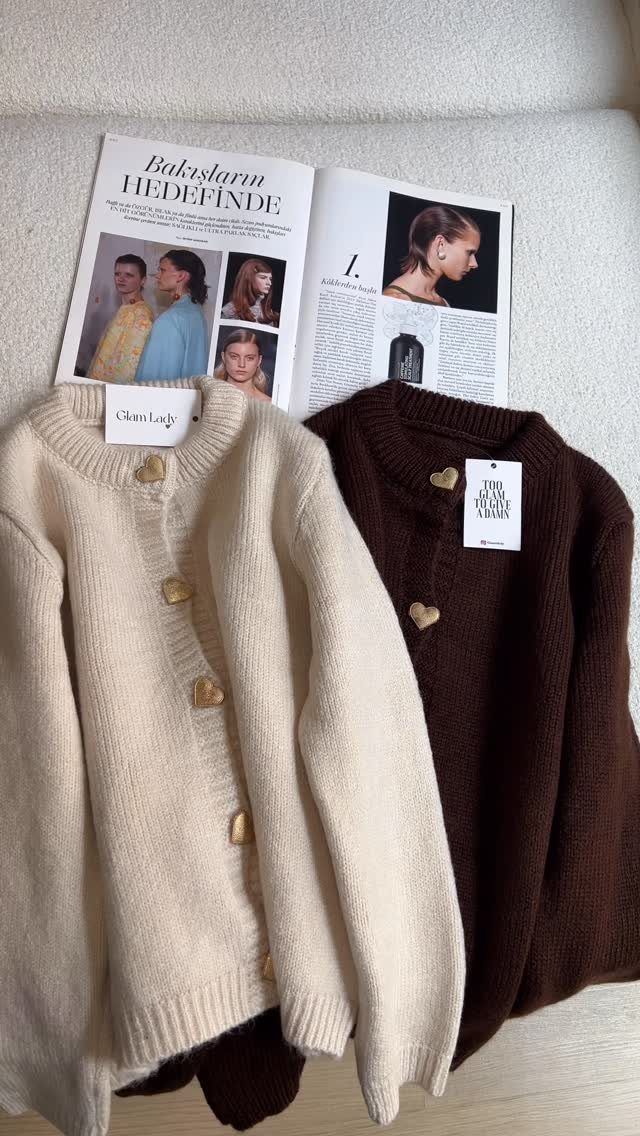 Cream and brown knit cardigans with heart buttons resting next to an open fashion magazine.