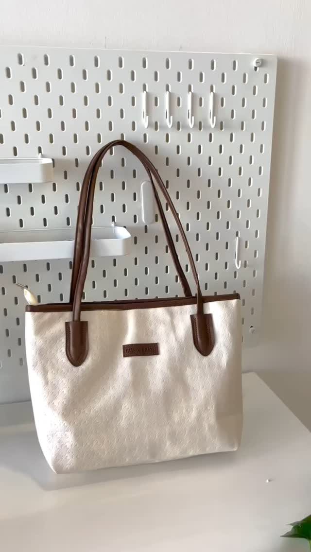 Cream canvas tote bag with brown leather handles resting on a white desk.