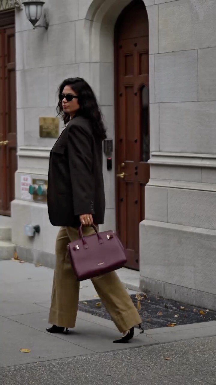 Woman walking in a city wearing a dark blazer and tan wide-leg tailored pants.