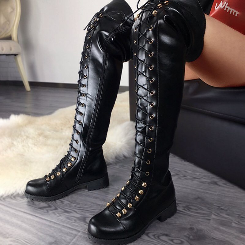 Black lace-up tall leather boots with gold eyelets on a grey floor.