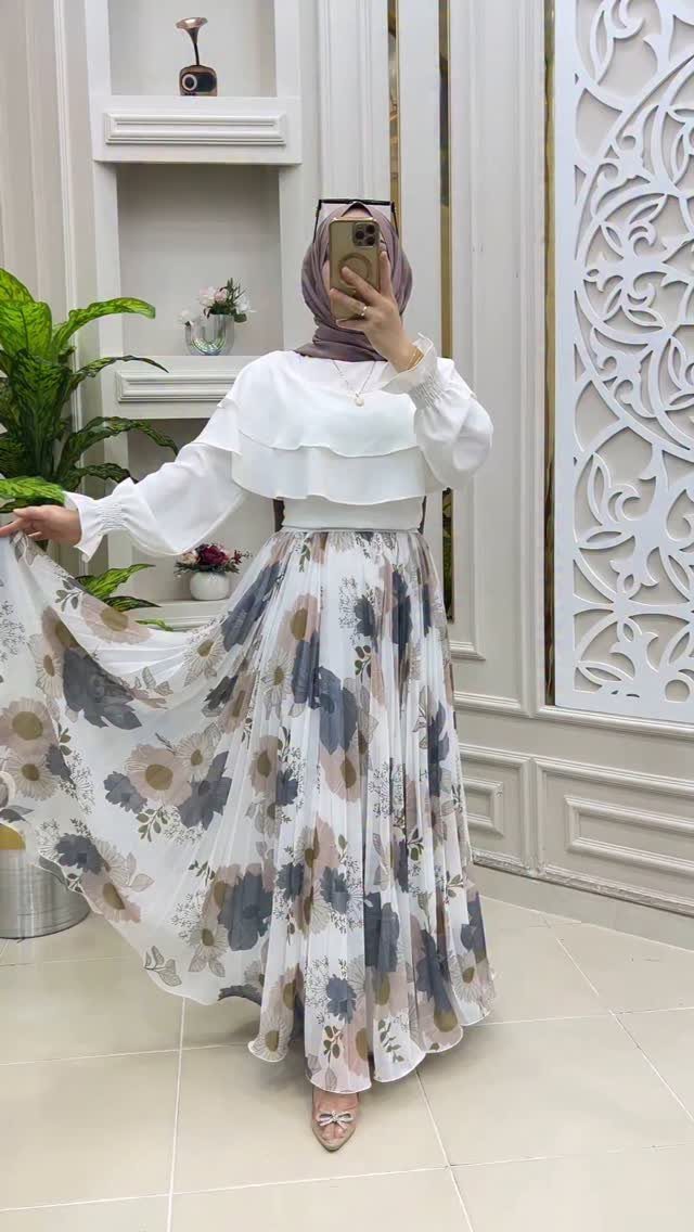 Woman posing in a white blouse and a floral patterned maxi skirt.