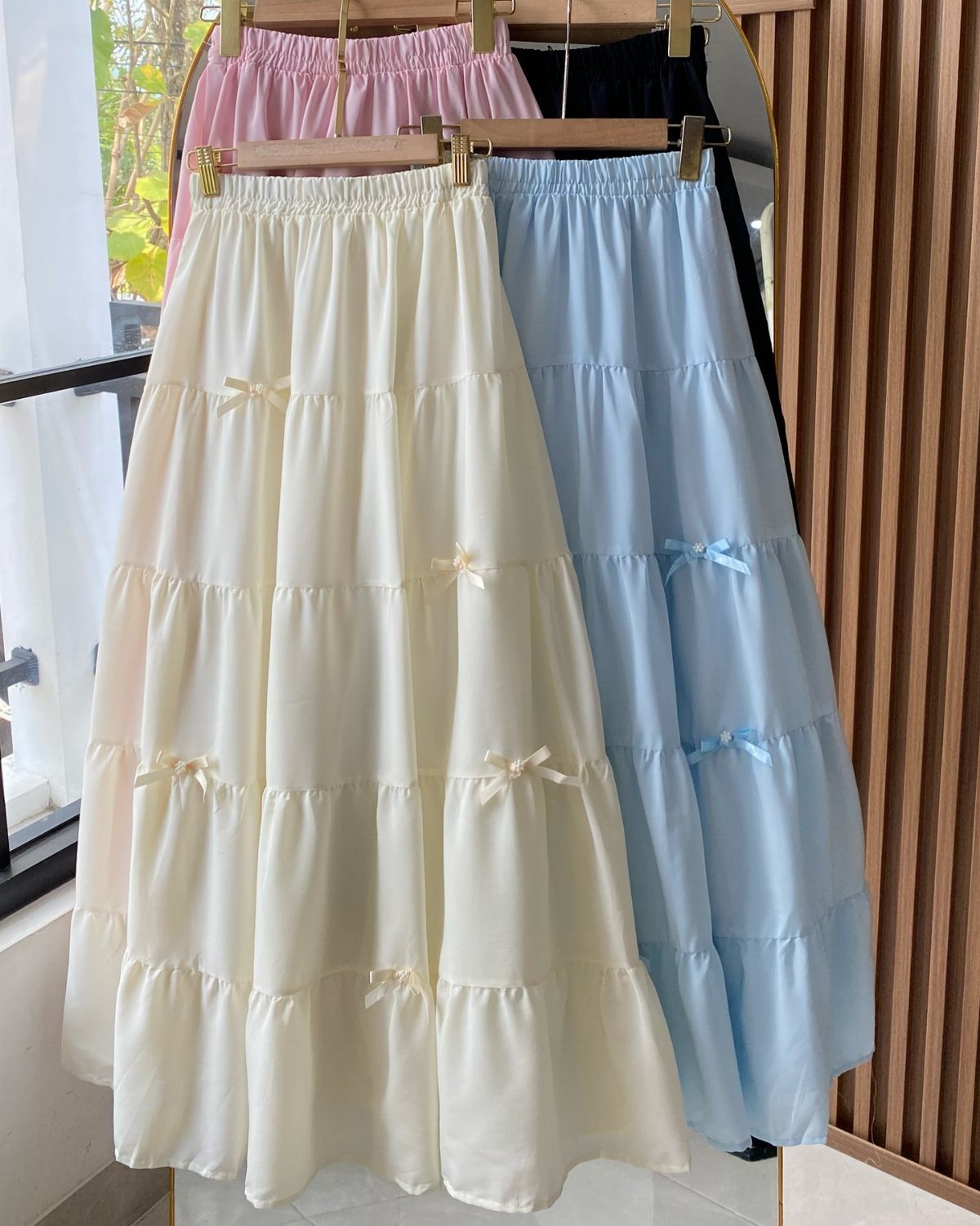 Three tiered long skirts in cream, blue, and pink hanging on gold hangers.