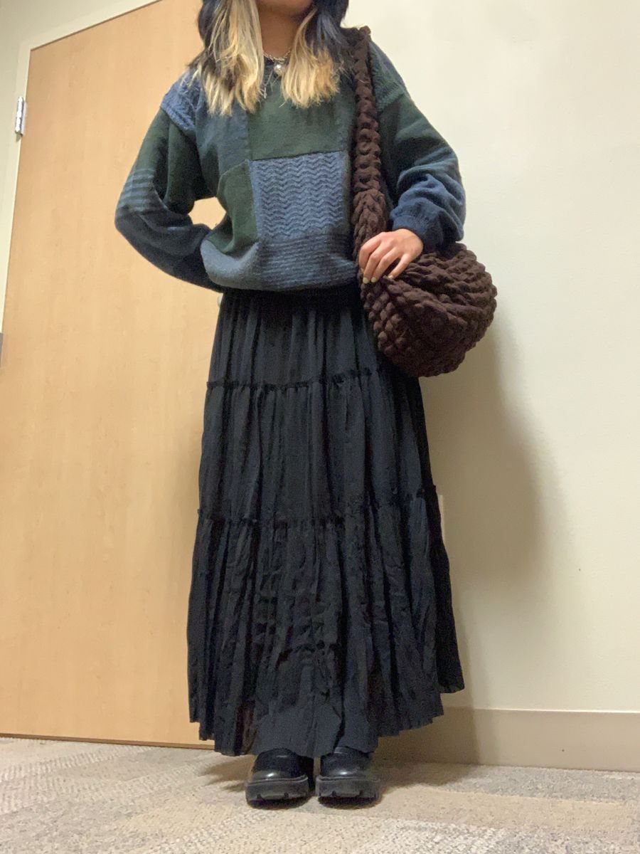 A person wearing a patchwork chunky sweater paired with a long black tiered maxi skirt.