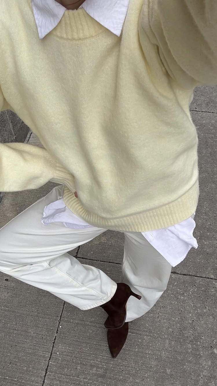 Person wearing a yellow sweater, white collared shirt, white pants, and brown heels on a sidewalk.