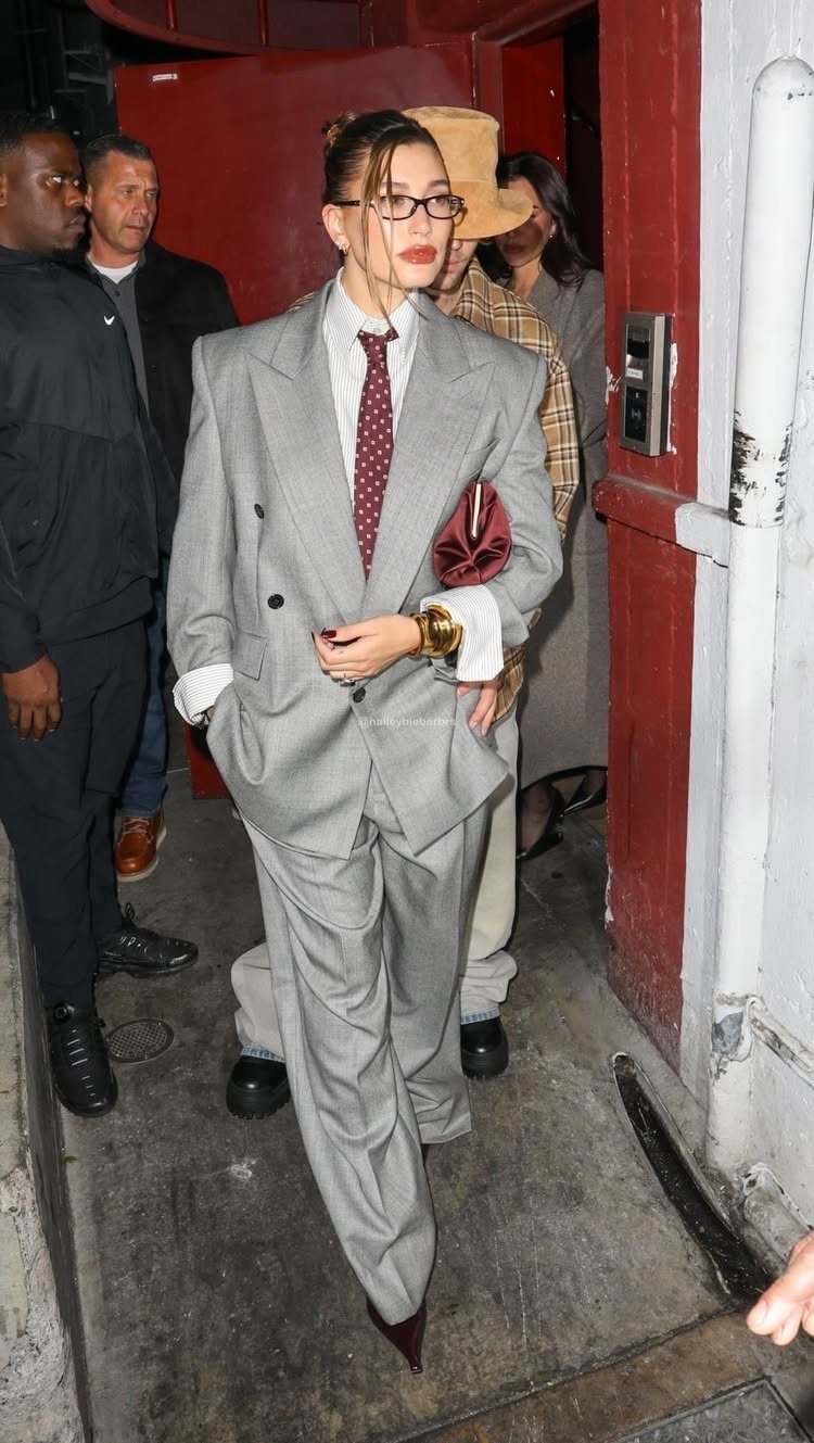 Woman in an oversized grey power suit, white shirt, and red tie walking outdoors.