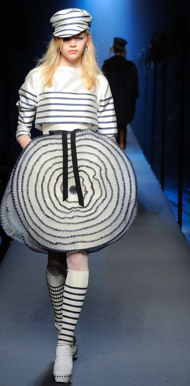 Model walking a runway in avant-garde navy and white striped clothing and a large circular skirt.
