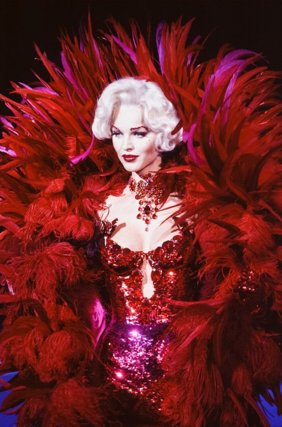 Woman in a dramatic red sequined bodysuit with massive red feather plumage.
