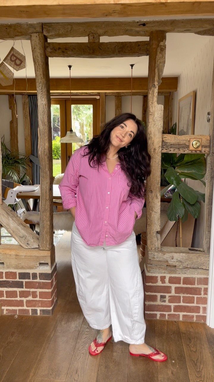 Woman posing in a pink striped shirt, white wide-leg pants, and red flip-flops.